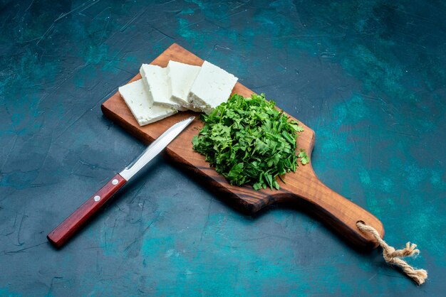 Vista superior de queso blanco con verduras frescas sobre superficie azul oscuro