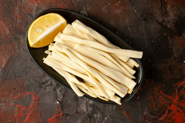 Vista superior de queso en rodajas con trozo de limón dentro de la placa sobre fondo oscuro