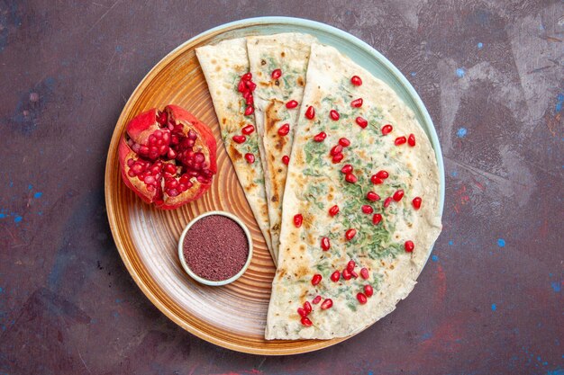 Vista superior qutabs deliciosos trozos de masa cocida con verduras y granadas en el plato de cocina de cena de cena de masa de superficie oscura