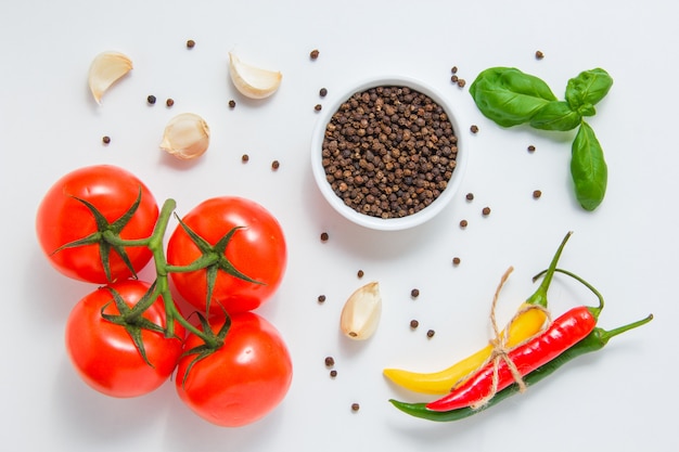 Vista superior racimos de tomates con un tazón de pimienta negra, ajo, hojas, ají sobre fondo blanco. horizontal