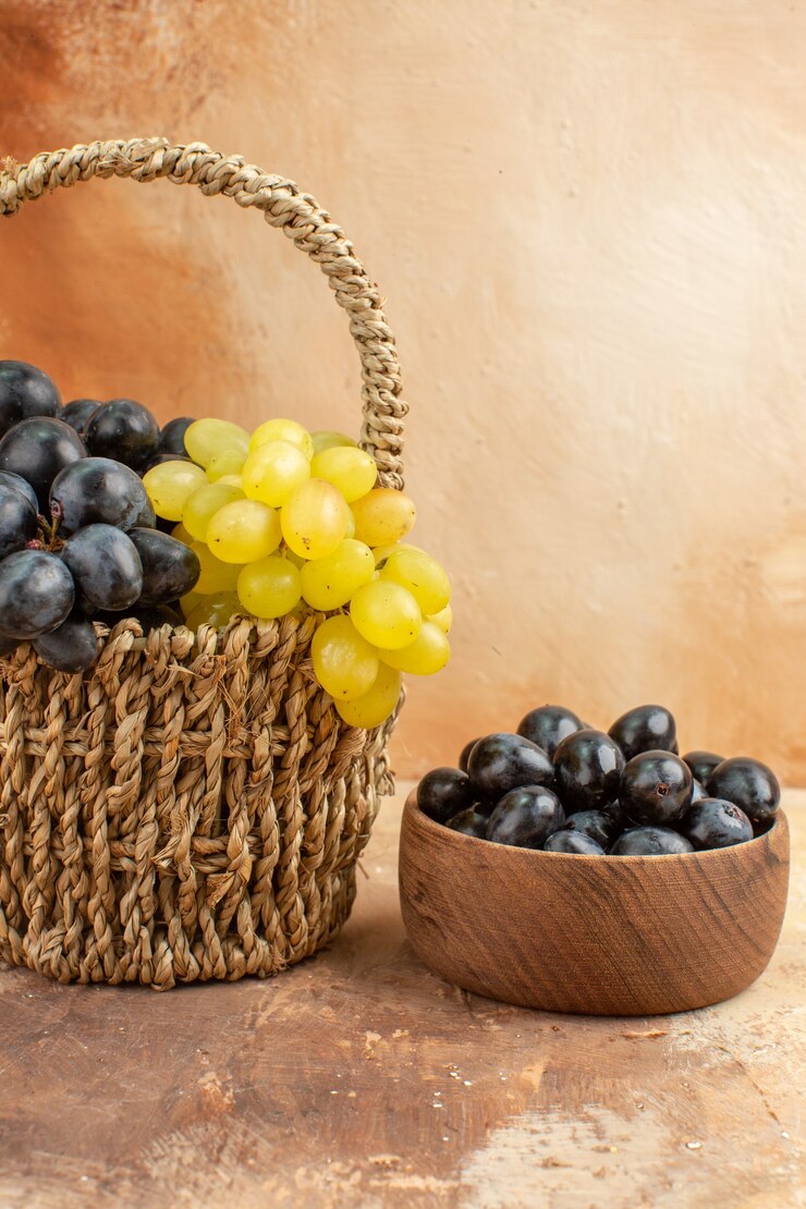 Foto gratuito vista superior de racimos de uvas amarillas y negras en una canasta de madera y en una pequeña olla marrón