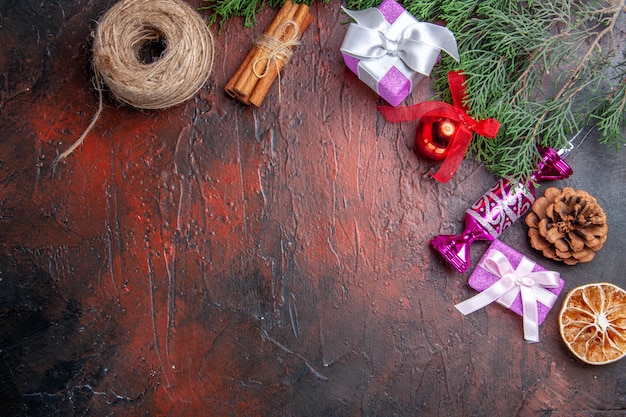 Vista superior rama de árbol de regalos de navidad con cono de árbol de navidad juguetes hilo de paja de canela en superficie roja oscura