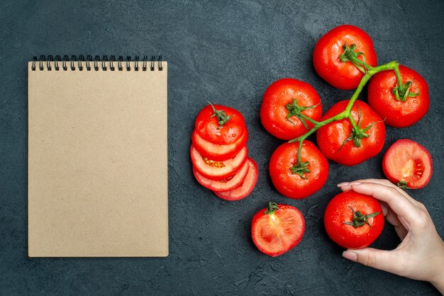 Vista superior de la rama de tomate fresco tomates picados tomate rojo en el cuaderno de mano femenina en el cuadro negro