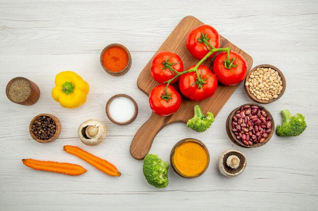 Vista superior de la rama de tomate en la tabla de cortar hongos brócoli frijoles cuencos cuencos de pimiento con especias en la mesa