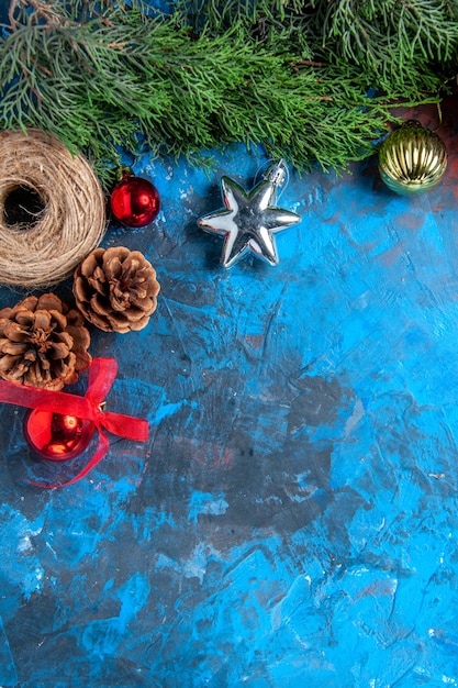 Vista superior de las ramas de los árboles de pino con piñas, juguetes de navidad de hilo de paja en una superficie azul-roja