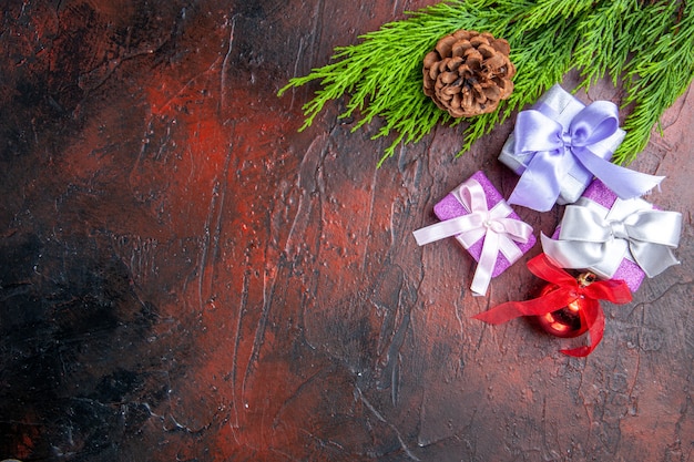 Vista superior de las ramas de los árboles de regalos de Navidad con cono de juguete de árbol de Navidad sobre fondo rojo oscuro