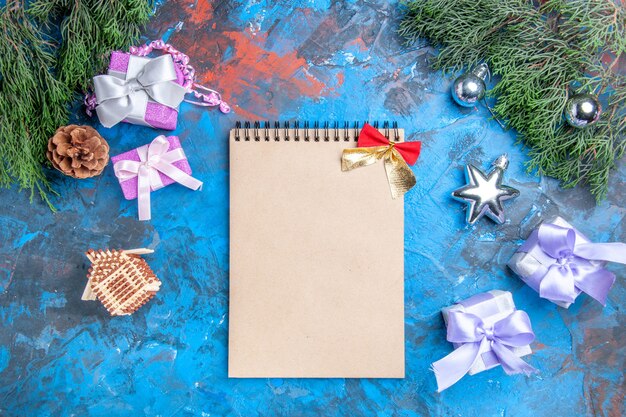 Vista superior de ramas de pino árbol de navidad juguetes regalos de navidad cuaderno con pequeño lazo sobre fondo azul-rojo