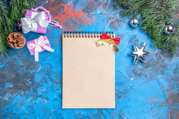 Vista superior de ramas de pino árbol de navidad juguetes regalos de navidad cuaderno sobre fondo azul-rojo