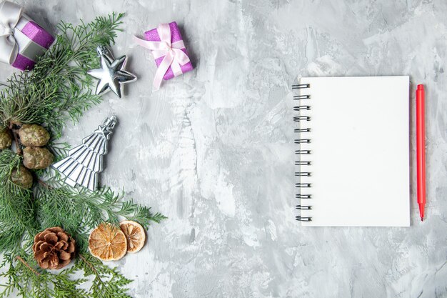 Vista superior de ramas de pino cuaderno lápiz rojo piñas pequeños regalos sobre fondo gris espacio de copia