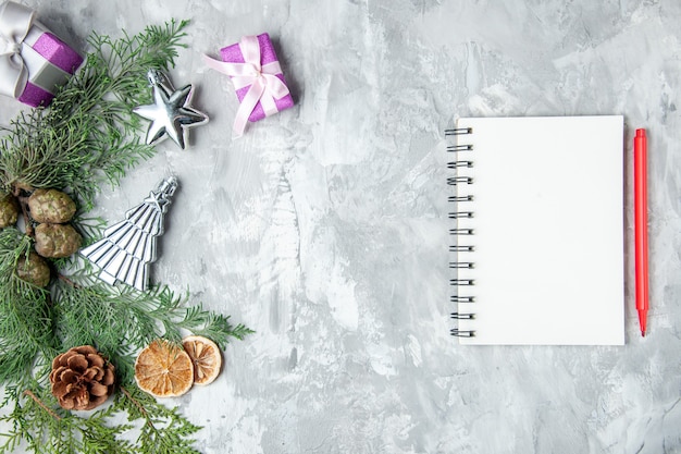 Vista superior de ramas de pino cuaderno lápiz rojo piñas pequeños regalos en superficie gris