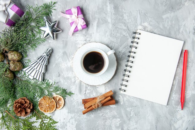 Foto gratuita vista superior de ramas de pino cuaderno lápiz rojo taza de té canela piñas pequeños obsequios sobre fondo gris