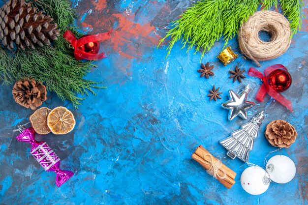 Vista superior ramas de pino hilo de paja juguetes de árbol de navidad semillas de anís palitos de canela rodajas de limón secas en superficie azul-roja