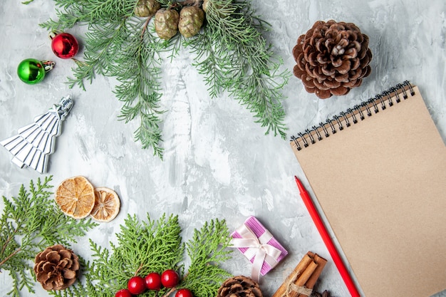 Vista superior ramas de pino pequeños regalos árbol de navidad juguetes cuaderno lápiz sobre fondo gris