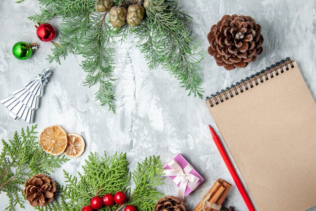 Vista superior ramas de pino pequeños regalos árbol de navidad juguetes cuaderno lápiz sobre fondo gris