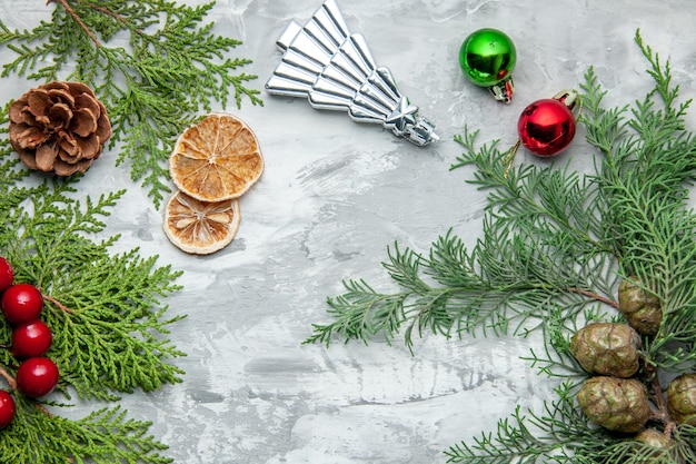 Vista superior ramas de pino pequeños regalos juguetes de árbol de navidad rodajas de limón secas sobre superficie gris