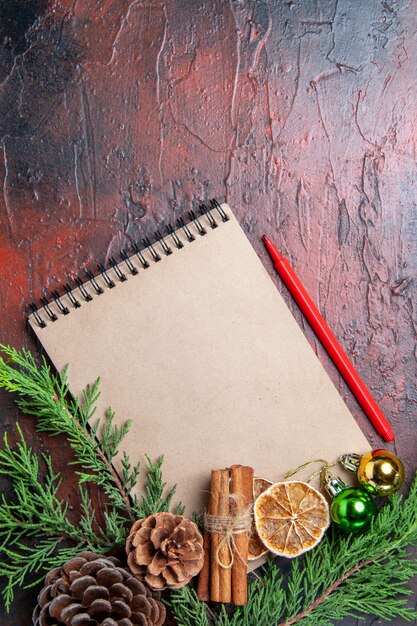 Vista superior de ramas de pino y piñas en un cuaderno rojo bolígrafo rodajas de limón seco canela en la superficie de color rojo oscuro espacio libre