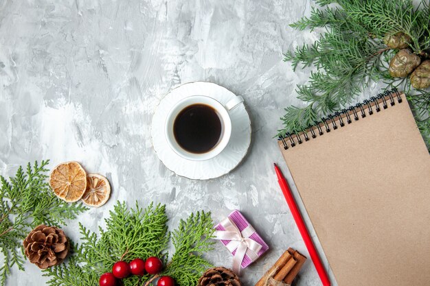 Foto gratuita vista superior ramas de pino taza de té pequeños regalos árbol de navidad juguetes cuaderno lápiz sobre superficie gris