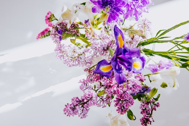Vista superior de un ramo de flores lilas con color blanco alstroemeria iris morado oscuro y flores de statice en un jarrón de vidrio sobre fondo blanco.