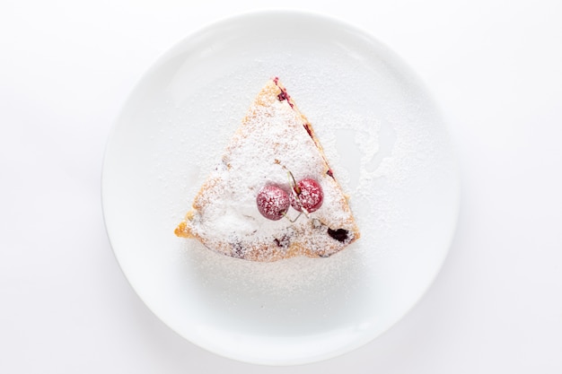 Vista superior de la rebanada de pastel de cereza dentro de la placa blanca con azúcar en polvo sobre el fondo blanco hornear masa dulce de galleta de pastel