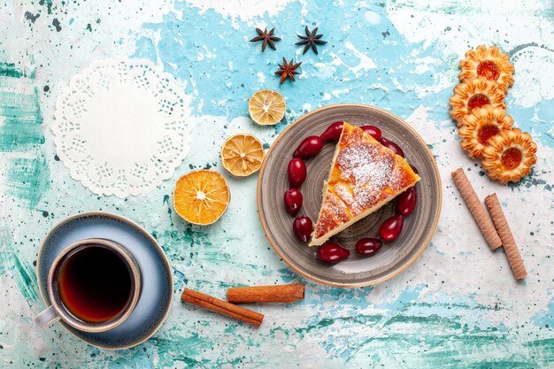 Vista superior de la rebanada de pastel con galletas y una taza de té en el escritorio azul pastel de frutas hornear pastel galleta dulce