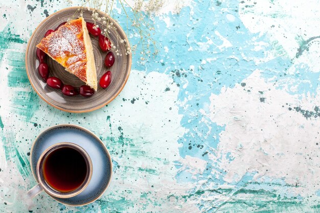 Vista superior de la rebanada de pastel ingenio cornejos rojos frescos y una taza de té sobre fondo azul pastel de frutas hornear tarta de azúcar galleta dulce