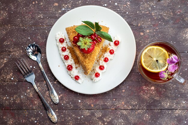 Vista superior de una rebanada de pastel de miel con arándanos dentro de un plato blanco con té en el fondo oscuro pastel de té