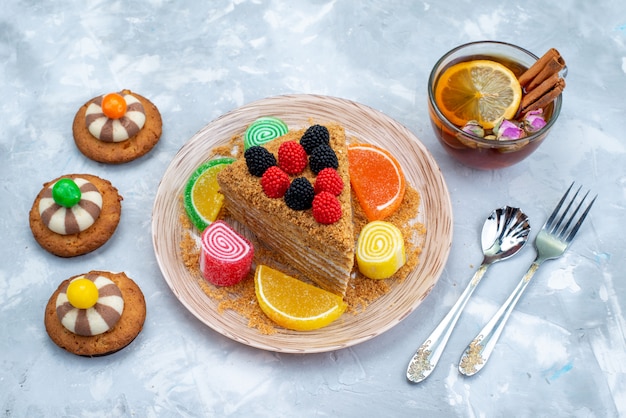 Una vista superior rebanada de pastel de miel dentro de la placa con dulces, galletas y té en el escritorio azul pastel de té de galletas hornear