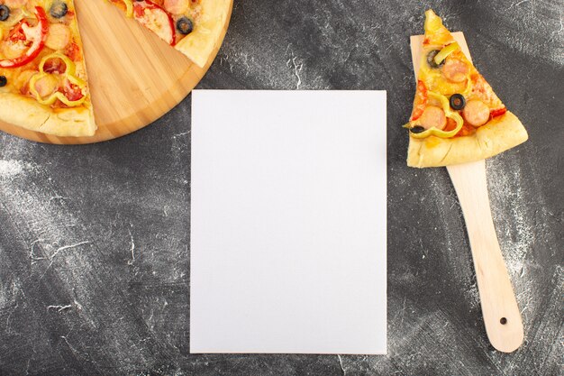 Vista superior rebanada de pizza con aceitunas negras, tomates y salchichas en la cuchara de madera cerca de papel vacío en blanco en el escritorio gris comida comida de pizza de masa italiana