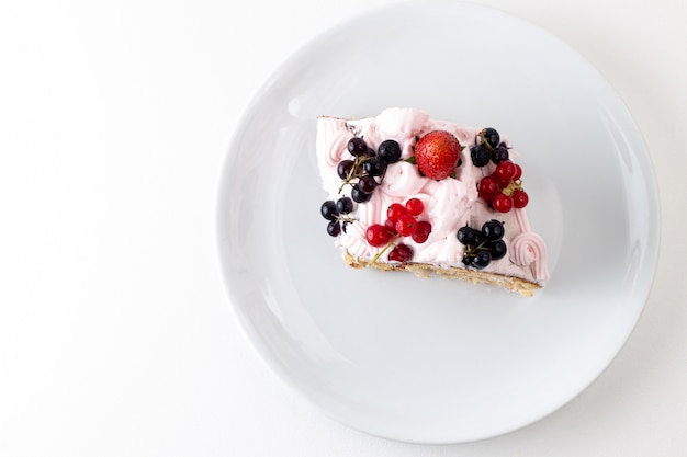 Vista superior de la rebanada de rollo con crema de arándanos y fresa dentro de la placa blanca sobre el fondo blanco pastel de galleta color dulce