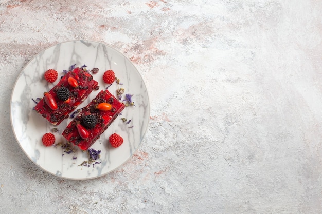 Vista superior rebanadas de pastel de bayas con glaseado cremoso rojo y bayas frescas sobre superficie blanca