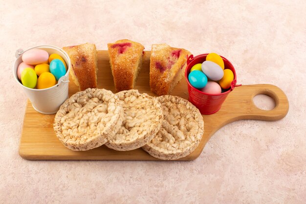 Una vista superior de las rebanadas de pastel de cereza con dulces y galletas en el escritorio rosa pastel de azúcar