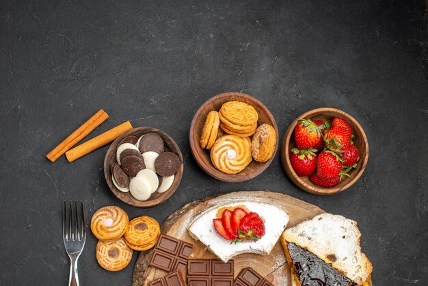 Vista superior de las rebanadas de pastel con galletas y chocolate sobre fondo oscuro