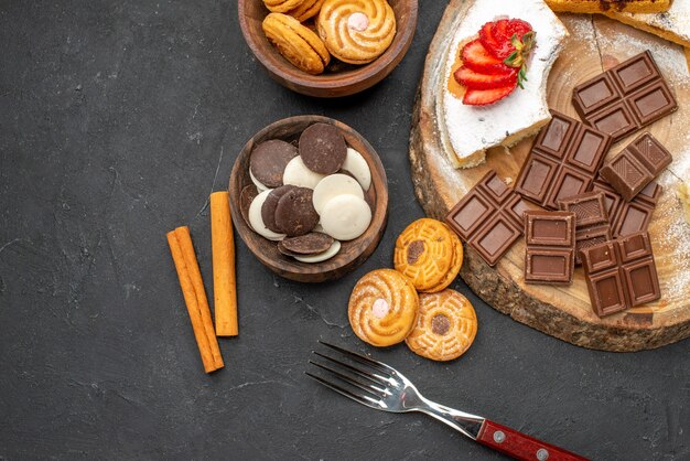 Vista superior de las rebanadas de pastel con galletas y chocolate sobre fondo oscuro