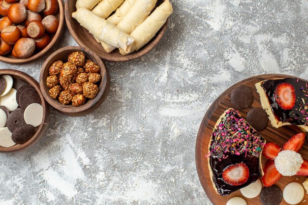 Vista superior de las rebanadas de pastel con galletas y dulces en la superficie blanca