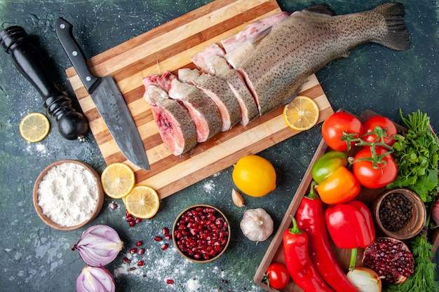 Vista superior de rebanadas de pescado crudo cuchillo en tabla de cortar verduras en madera tablero de servir molinillo de pimienta en la mesa de la cocina