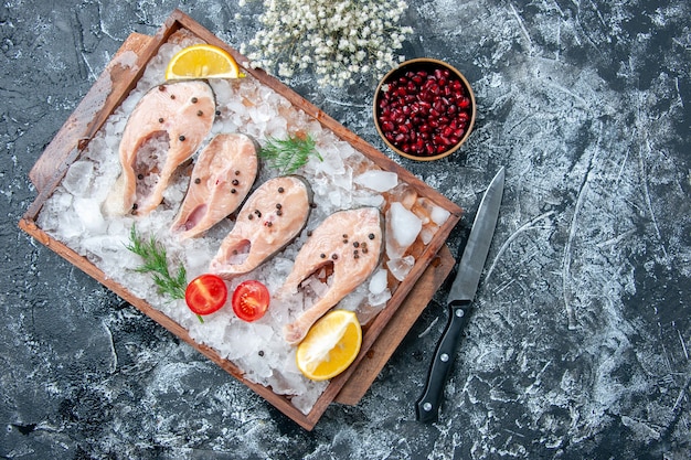 Vista superior rebanadas de pescado crudo con hielo en tablero de madera, cuchillo, semillas de granada en un tazón pequeño en el lugar de la copia de la mesa