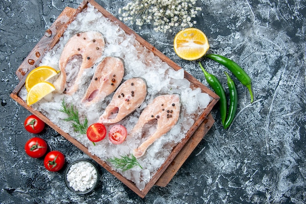 Vista superior de las rebanadas de pescado crudo con hielo en el tablero de madera, sal marina en un tazón pequeño, verduras en la mesa