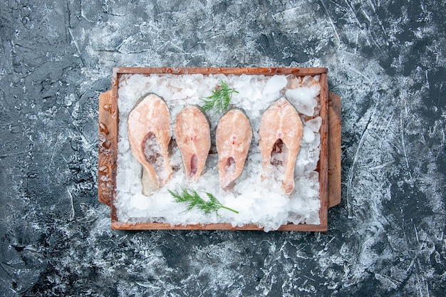 Vista superior rebanadas de pescado crudo con hielo en tablero de madera sobre fondo gris