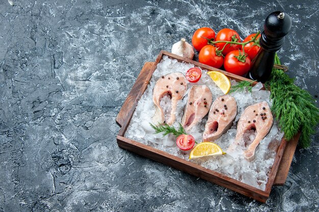 Vista superior rebanadas de pescado crudo con hielo en tablero de madera tomates ajo eneldo en lugar de copia de mesa