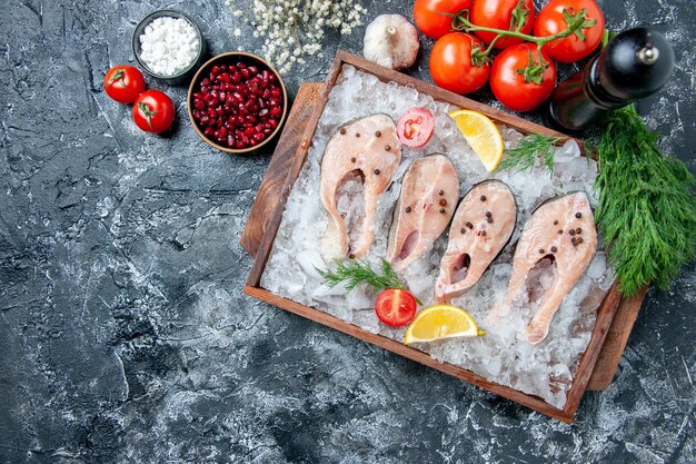 Vista superior rebanadas de pescado crudo con hielo en tablero de madera tomates ajo eneldo sal marina semillas de granada en tazones sobre mesa