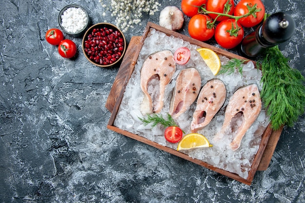 Vista superior rebanadas de pescado crudo con hielo en tablero de madera tomates ajo eneldo sal marina semillas de granada en tazones sobre mesa