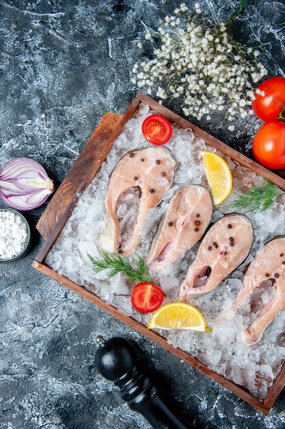 Vista superior rebanadas de pescado crudo con hielo en tablero de madera tomates cebolla en mesa