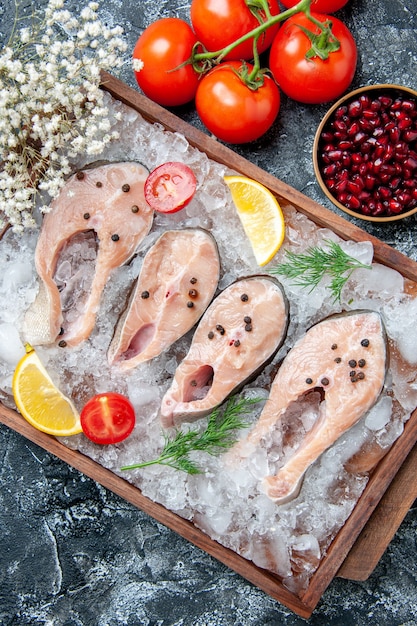 Vista superior rebanadas de pescado crudo con hielo en tazones de madera con semillas de granada tomates en la mesa