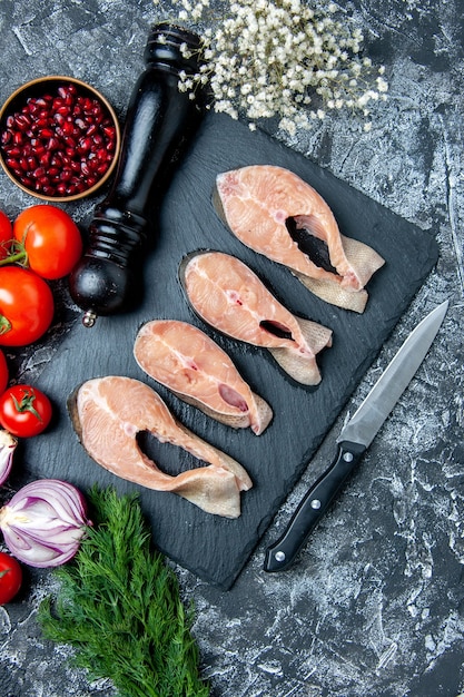 Vista superior rebanadas de pescado crudo en tablero negro eneldo semillas de granada tomates molinillo de pimienta en la mesa