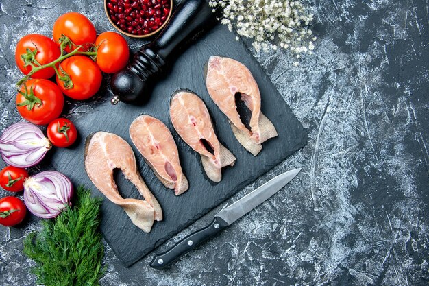 Vista superior rebanadas de pescado crudo en tablero negro semillas de granada eneldo tomates cuchillo molinillo de pimienta en el lugar de la copia de la mesa