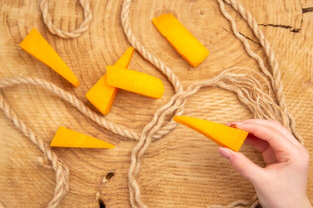 Vista superior rebanadas de queso queso de cuerda en mano femenina sobre mesa de madera