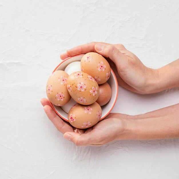 Vista superior del recipiente con huevos de Pascua decorados en las manos