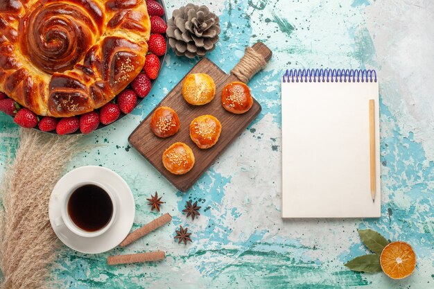 Vista superior redonda deliciosa tarta con tartas de fresas y taza de té en la superficie azul claro