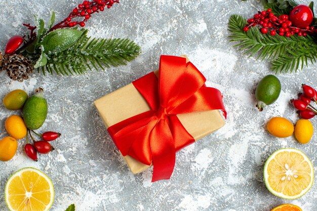 Vista superior de regalo de Navidad atado con cinta roja corta limones feijoas en mesa gris