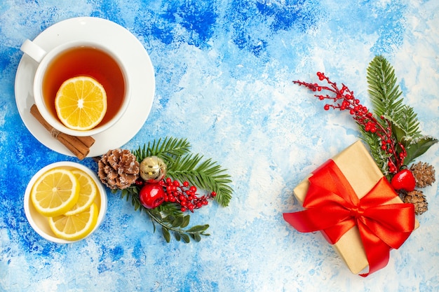 Vista superior de regalo de Navidad atado con cinta roja rama de árbol de Navidad una taza de té en la mesa azul